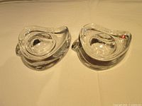 Two clear glass bird-shaped egg cups side by side on a beige surface with visible partial Finnish flag label.