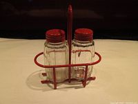 Front view of the glass salt and pepper shakers with red metal lids sitting in the red metal wire basket