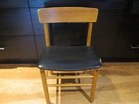 Front view of mid century dining chair with wooden backrest and black vinyl seat.