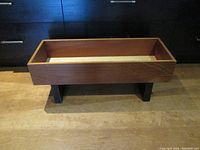 Angle view of rectangular wood planter/storage unit with black rectangular legs on a wood floor.