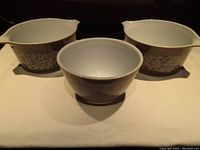 Three Pyrex Woodland pattern bowls, one 401 mixing bowl and two 473-B Cinderella bowls, shown with white interiors and brown exteriors decorated with white floral design.