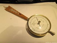 Full view showing the brass barometer circle attached to wooden handle with thermometer tube visible.