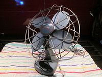 Front view of vintage Electrohome metal table fan showing four metal blades enclosed in a circular metal cage with front badge.