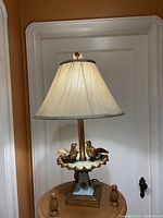 Full view of the whimsical bird table lamp showing the two birds on the scalloped base and pleated beige lamp shade.
