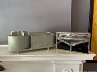 Photo of a green plastic cosmetic organizer with a spindle rotating caddy and drawer next to a mirrored glass box with ornate metal framing.