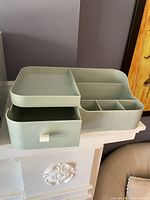 Photo showing two green cosmetic organizers stacked with compartments and drawers visible, on white surface.