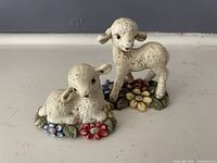 Photo of two Goebel porcelain lamb figurines, one standing and one lying on a floral base, showing detail and condition.