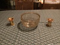 Glass bowl with removable insert sitting between two gold-colored candlesticks on patterned tablecloth