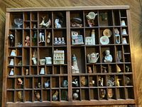 Top-down view of wooden display case with multiple small miniatures arranged in compartments, including the Swarovski clam shell and swan figurines