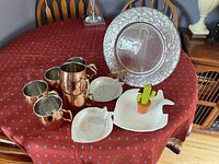 Full view of coral glass serving plate with silver-tone decorative rim alongside two white fish plates, cactus tea diffuser, and five Moscow Mule mugs on red patterned tablecloth.