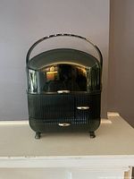 Front view of rounded green plastic cosmetic styler showing curved handle and two drawers at the base.