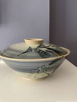 Pottery bowl viewed from side with lid on showing blue-gray glaze and daisy flower design.