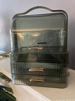 Front view of the square green translucent plastic cosmetic styler organizer showing the carrying handle and three drawers with gold-tone handles.