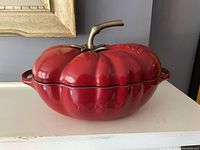 Staub cast iron cocotte shaped like a red pumpkin with bronze stem handle, closed.