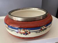 Side view showing decorative fruit pattern, blue band, and red-orange rim with silver metal band on top