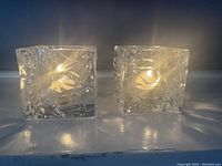 Two clear textured glass votive candle holders lit with tealight candles, showing soft warm glow and frosted ice-like texture