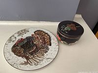 Turkey-themed trivet beside the small lidded bowl with fall vegetable decoration on lid