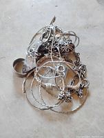Image showing tangled scrap sterling silver jewelry parts including chains, rings, and earrings on a light surface.