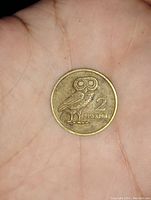 Front side of a 2 Drachmai Greek coin with owl design held in hand showing detail and size.