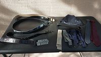 Three belts including one black leather, one smaller black leather, and one wide black Star Wars belt, arranged on left side of table.