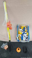 Street hockey stick with attached orange balls and rubber pucks shown alongside plastic container of flag football belts.