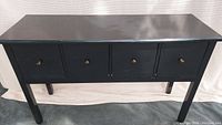 Front view of the 4 drawer black console/entry way table showing all four drawers with visible small round brass knobs and distressed edges.