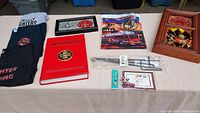 Full lot showing all items on table: three folded firefighter T-shirts, two clocks, red collectible book, yard flag, magnetic photo frame, lighter