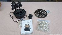 Photo showing the assembled fountain with power adapter, instruction manual, bag of clear beads, and black iron trivet arranged on a surface.