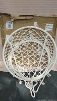 Large macrame hanging swing folded with visible circular frame and woven rope.