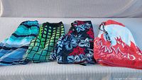 Four pairs of men's swim trunks displayed side by side showing different colors and patterns including blue stripes, green grid, floral, and flame designs.