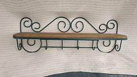 Front view of vintage kitchen shelf showing wood top and decorative dark green metal scrollwork with four hooks below.