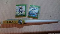 Two Xbox One football games and a Wii lightsaber controller holder laid out on fabric.