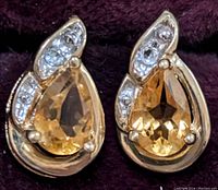 Front view of the pair of 10K yellow gold earrings with pear-shaped faceted citrine gems and three small diamond accents on each earring.