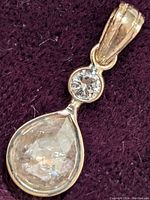 Front view of pendant on dark purple fabric showing pear-shaped fancy color diamond beneath round brilliant diamond.