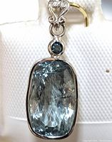 Close-up photo showing the light blue rectangular aquamarine with faceted cut and small round blue diamond above it in 14K gold setting.