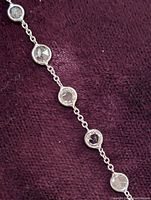 Close-up of five of the six bezel-set round diamonds on the chain against purple background