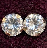 Close-up front view of the pair of 14K gold stud earrings with round cubic zirconia stones on dark fabric background.