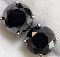 Close-up view of two round faceted black diamonds in four-prong settings