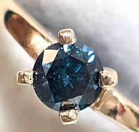 Front-facing view of the round blue diamond in four-prong yellow gold setting.