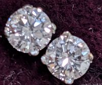 Close-up photo of two round brilliant cut lab-grown diamonds set in 14K gold prong settings, displayed on dark background
