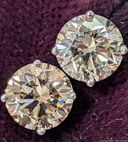 Close-up of both round diamonds set in four-prong settings on purple fabric.