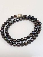 Full view of black pearl necklace with magnetic clasp coiled loosely on a white background.