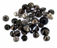 Multiple small round brilliant-cut black diamonds scattered on a white surface, showing faceted tops and varied sizes.