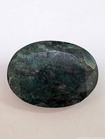 Top view of the genuine emerald, showing the top facets, oval shape, and dark green color with inclusions.