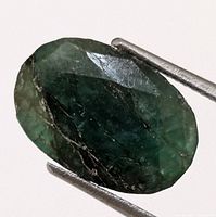 Front view of the dark green oval faceted emerald showing natural inclusions and internal fractures.