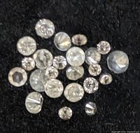 Close-up photo of multiple loose round cut diamonds on a black surface showing different sizes and facets.