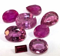 Close-up photo of eight loose faceted rubies in varied shapes and pink to red-purple shades, focused on showcasing size, cut, and color range.