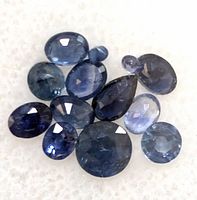Multiple faceted blue sapphires of various sizes and shapes displayed on white foam.