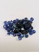 Close-up of assorted loose faceted sapphire gemstones in varying sizes and shades of blue, placed on a white background.