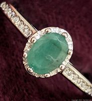 Close-up image of the oval emerald center stone with cubic zirconia halo and band accents on a sterling silver ring.